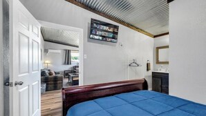 Une chambre à coucher comprenant un lit, un téléviseur fixé au mur, une armoire et une porte donnant sur une autre pièce.