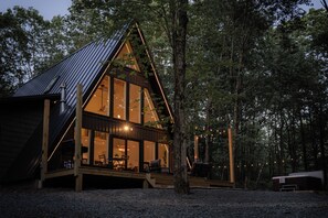 A cabin with a sloped roof, large windows, and a deck area. - Modern Luxury A-Frame in Woods w/Hot Tub, Sauna, Arcade, Gas Fireplace, Games (Albrightsville)