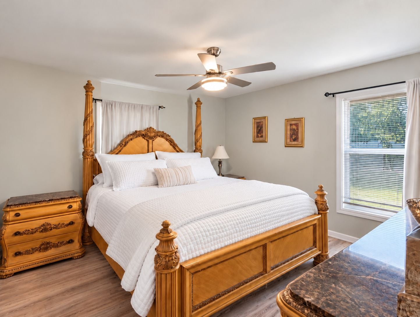 A bedroom with a four-poster bed, a nightstand, a dresser, a ceiling fan, and a window with blinds.