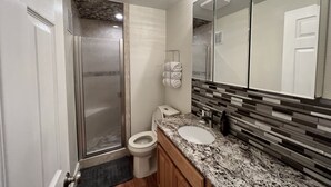 Ein modernes Badezimmer mit einer gläsernen Duschkabine, Toilette, Waschbecken mit Granitplatte und einem großen Spiegel.