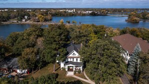 A large house with a porch, surrounded by dense trees and a lake.