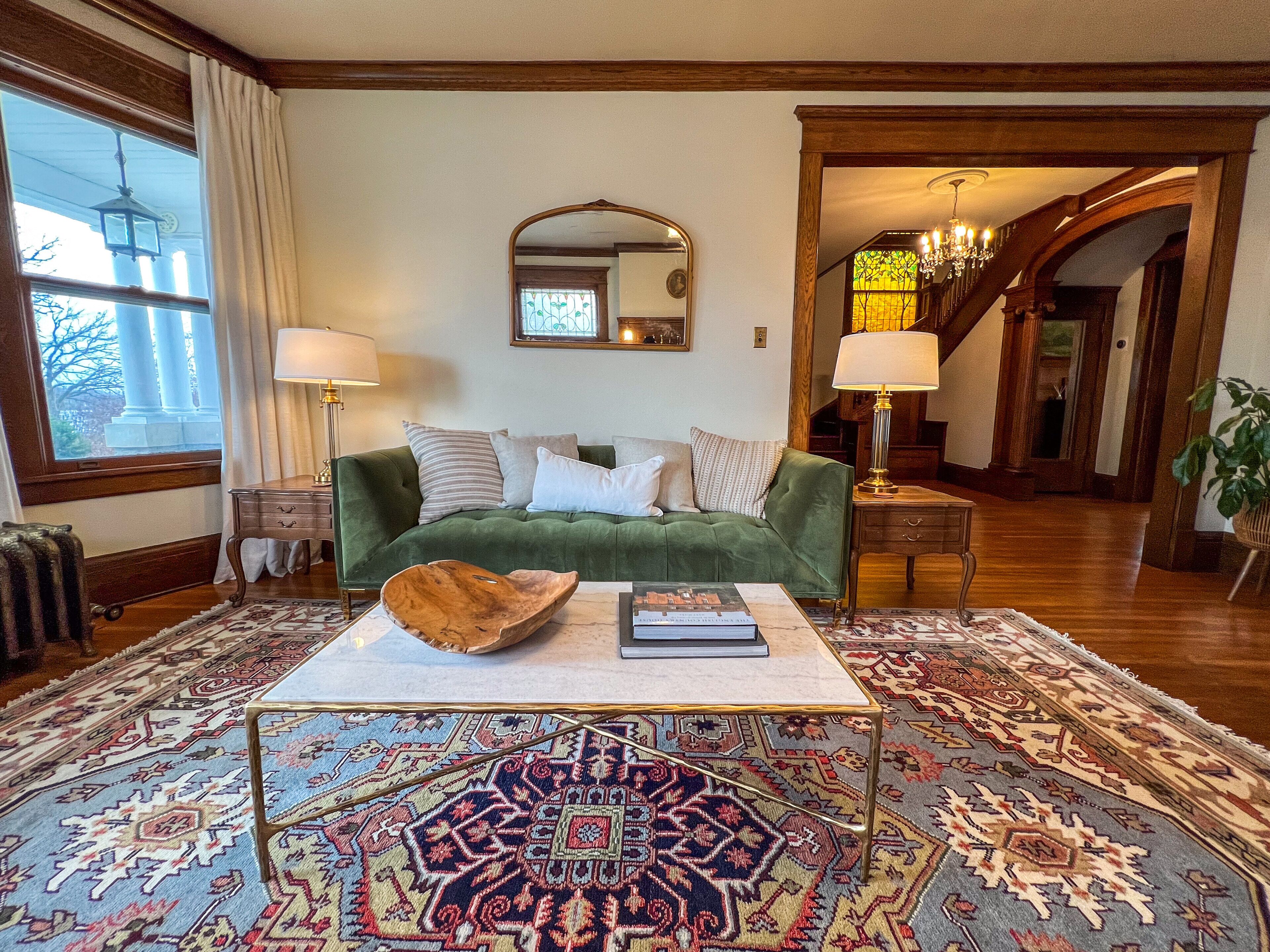 Una sala de estar con un sofá verde, una mesa de centro, alfombras estampadas y un espejo grande sobre el sofá.