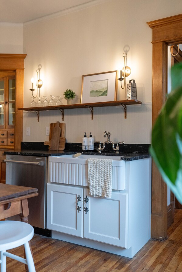 Cocina con isla blanca, armarios de madera, encimera negra y estante de madera sobre el lavabo.