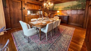 A dining area with a wooden table set for six, surrounded by chairs, a chandelier, and a painting on the wall.