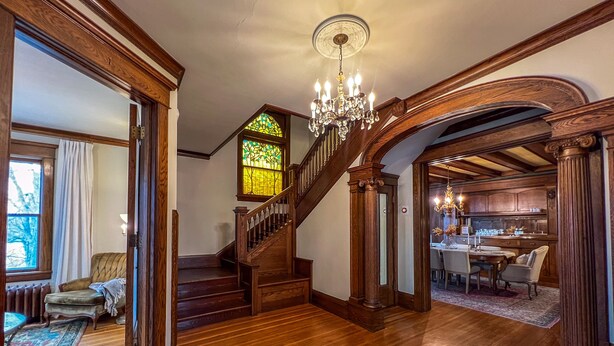 A grand staircase with a stained glass window, wooden flooring, and a chandelier.