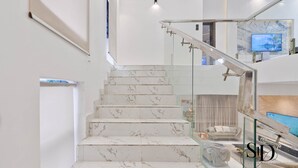A modern staircase with marble steps and glass railings, leading to a living area with a sofa and a television. -  Luxury 5 Bed Home with Swimming Pool, PS 5 Game,Snooker & Table Tenins in Lekki (Lekki)
