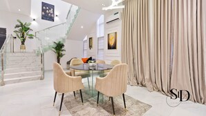 A modern dining area with a glass table, cushioned chairs, a staircase, and a large curtain. -  Luxury 5 Bed Home with Swimming Pool, PS 5 Game,Snooker & Table Tenins in Lekki (Lekki)