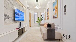 A modern living room with a flat-screen TV, a sofa, a coffee table, and a decorative plant. -  Luxury 5 Bed Home with Swimming Pool, PS 5 Game,Snooker & Table Tenins in Lekki (Lekki)