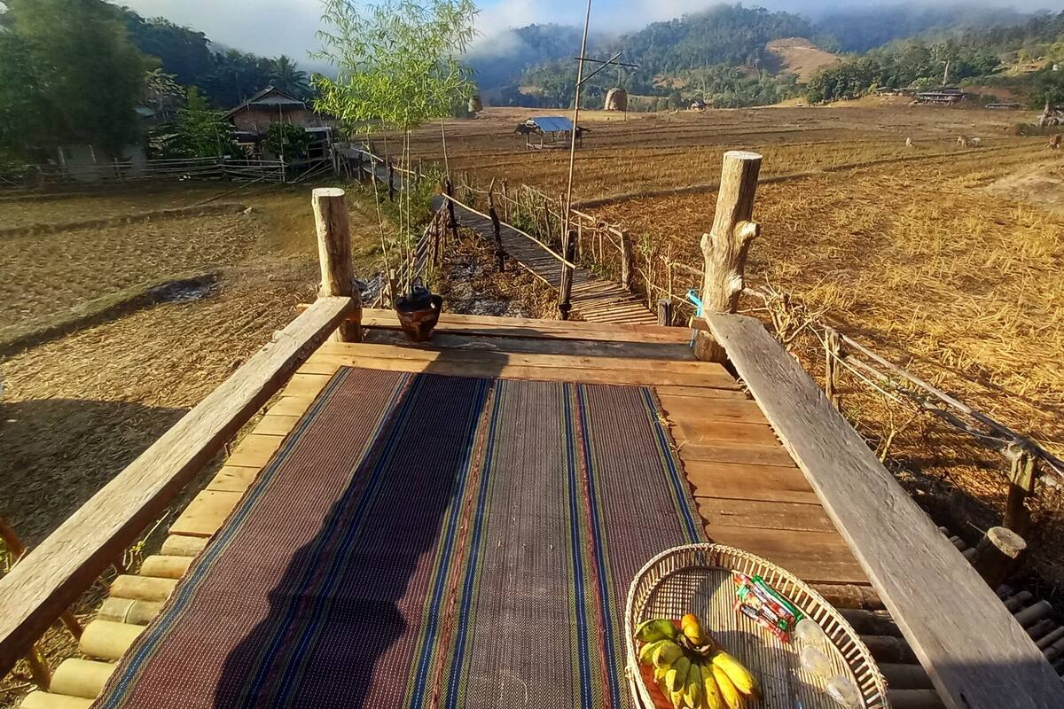 A wooden deck with a woven mat, a basket of bananas, and a small potted plant.