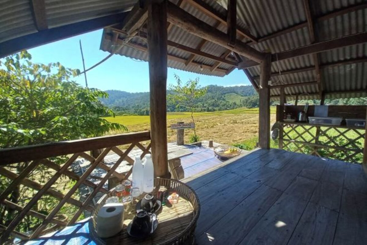 A covered outdoor area with a wooden deck, a wicker chair, and a table with various items.
