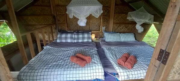 A cozy wooden cabin with two beds, each with a checkered bedspread and pillows, and a mosquito net above the beds. - Chinopuu Hut Homestay Muangkong (Chiang Dao)