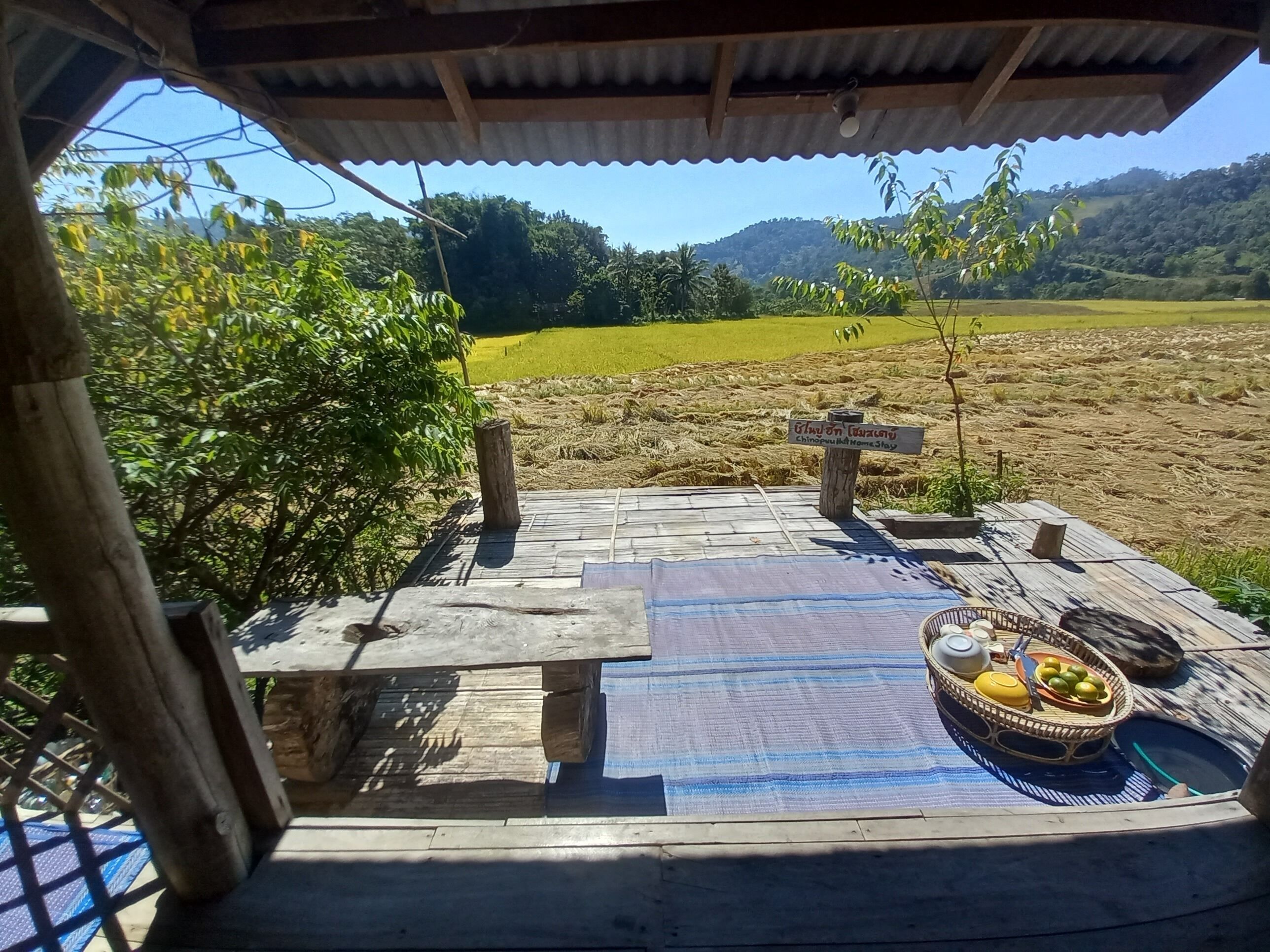 Una terraza de madera con una mesa y sillas, un cartel indicador y una mesa con frutas y una cesta.
