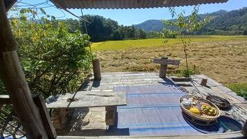 Una terraza de madera con una mesa y sillas, un cartel indicador y una mesa con frutas y una cesta.