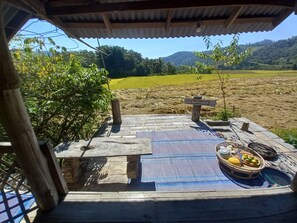 A wooden deck with a table and chairs, a signpost, and a table with fruits and a basket. - Chinopuu Hut Homestay  (Chiang Dao)