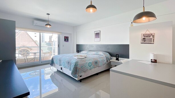 A modern bedroom with a large bed, a desk, and a view of the outside.