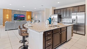 A modern kitchen with a central island, stainless steel appliances, and a dining area with a sofa and bar stools. - Fruit Ninja Arcade, Fast and Furious Racing, Space Bedrooms, Theater, Pool Table: Cosmic Way (Kissimmee)