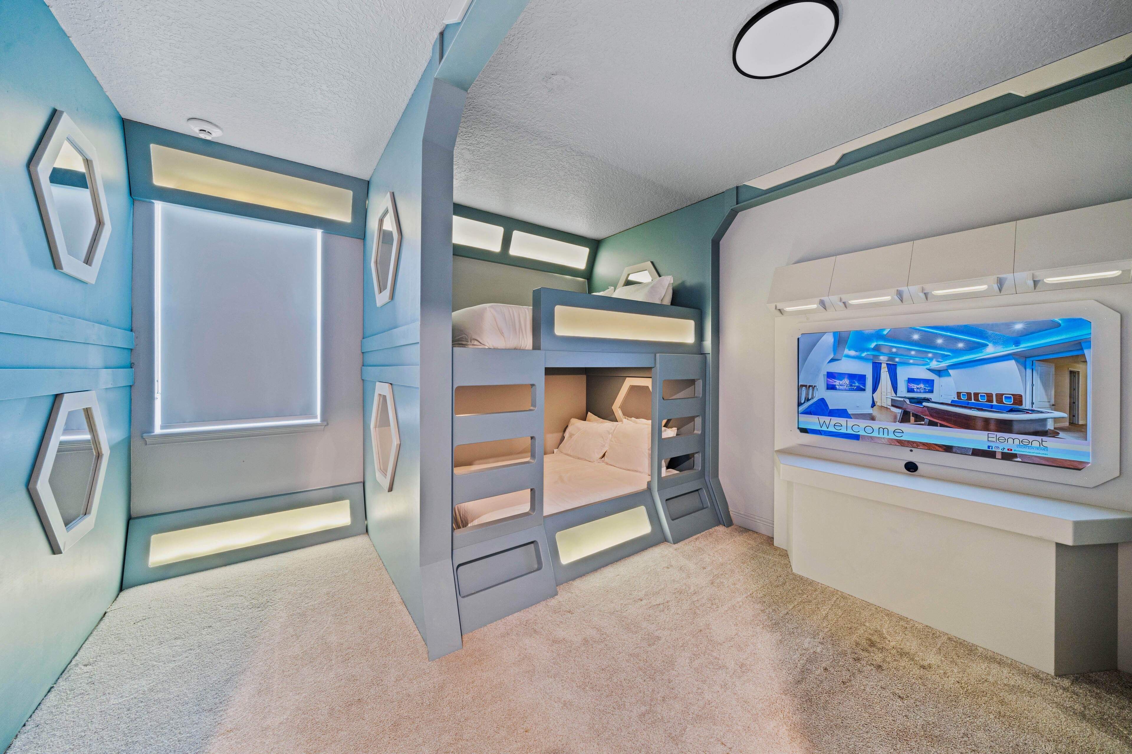 A room with bunk beds, a flat-screen TV, and a wall-mounted entertainment unit.