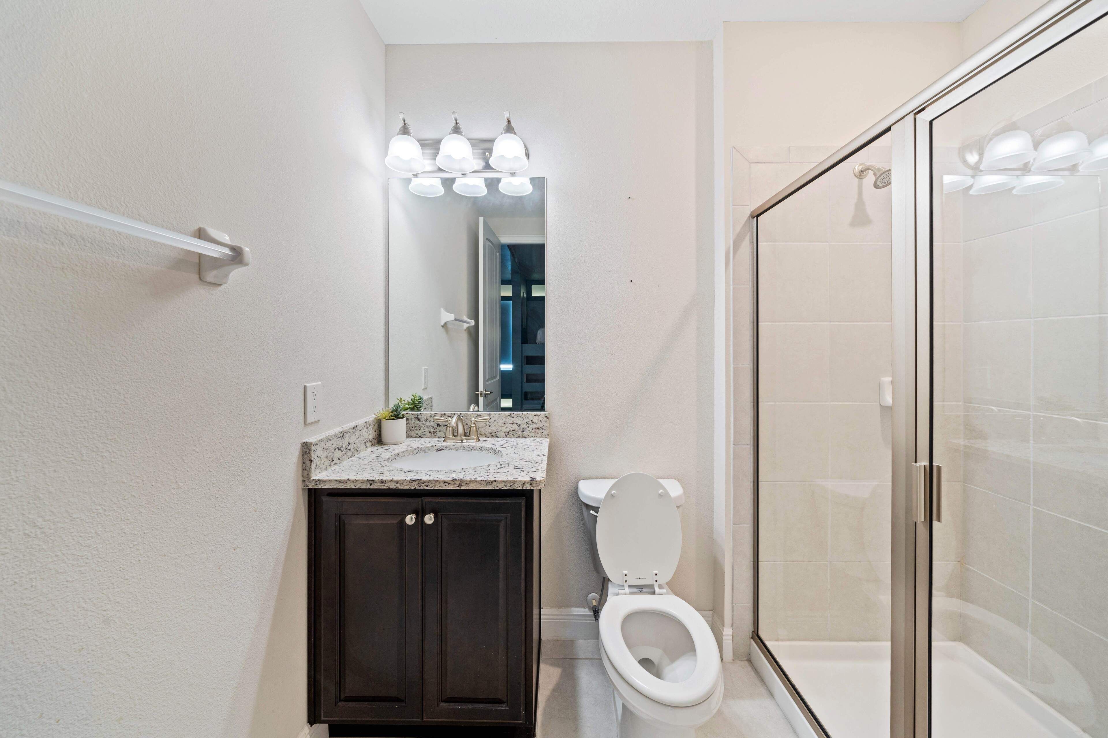 Une salle de bain comprenant des toilettes, un lavabo avec un plan de travail en granit, un miroir et une cabine de douche en verre.
