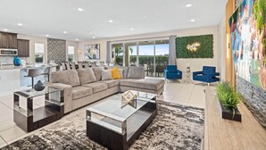 A modern living room with a sectional sofa, a glass coffee table, and a dining area with blue chairs. - Fruit Ninja Arcade, Fast and Furious Racing, Space Bedrooms, Theater, Pool Table: Cosmic Way (Kissimmee)