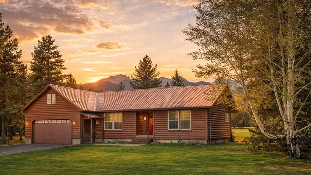Une cabane en rondins avec un garage, une véranda et une pelouse bien entretenue.