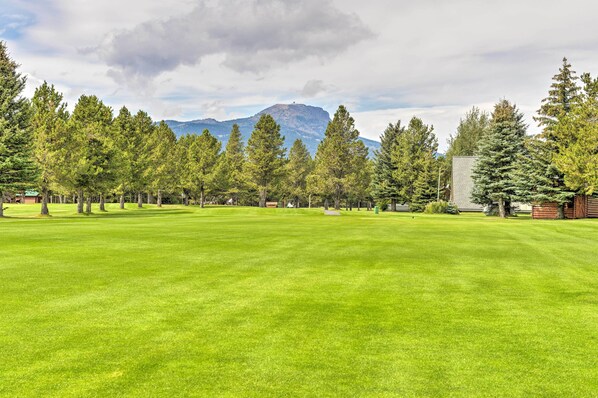 A well-maintained grassy area with a row of tall trees and a mountain in the background. - Island Park Cabin with Hot Tub • Summer escape •27 Min to Yellowstone (Island Park)