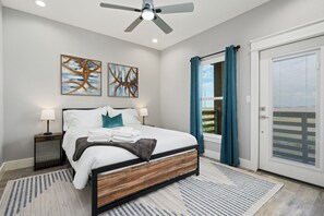 A bedroom with a bed, nightstands, ceiling fan, artwork, and a view through a window.