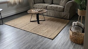 Uma sala de estar moderna com um sofá seccional, uma mesa de centro redonda e uma janela grande com cortinas.