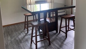 Uma sala de jantar com mesa de vidro rodeada por cadeiras de madeira, um candelabro e uma janela com cortinas.