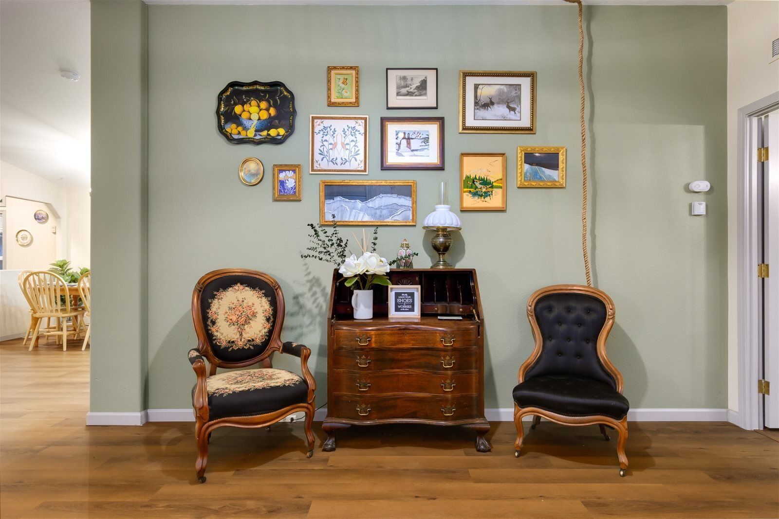 A room with two ornate chairs, a wooden dresser, and a wall adorned with framed pictures.