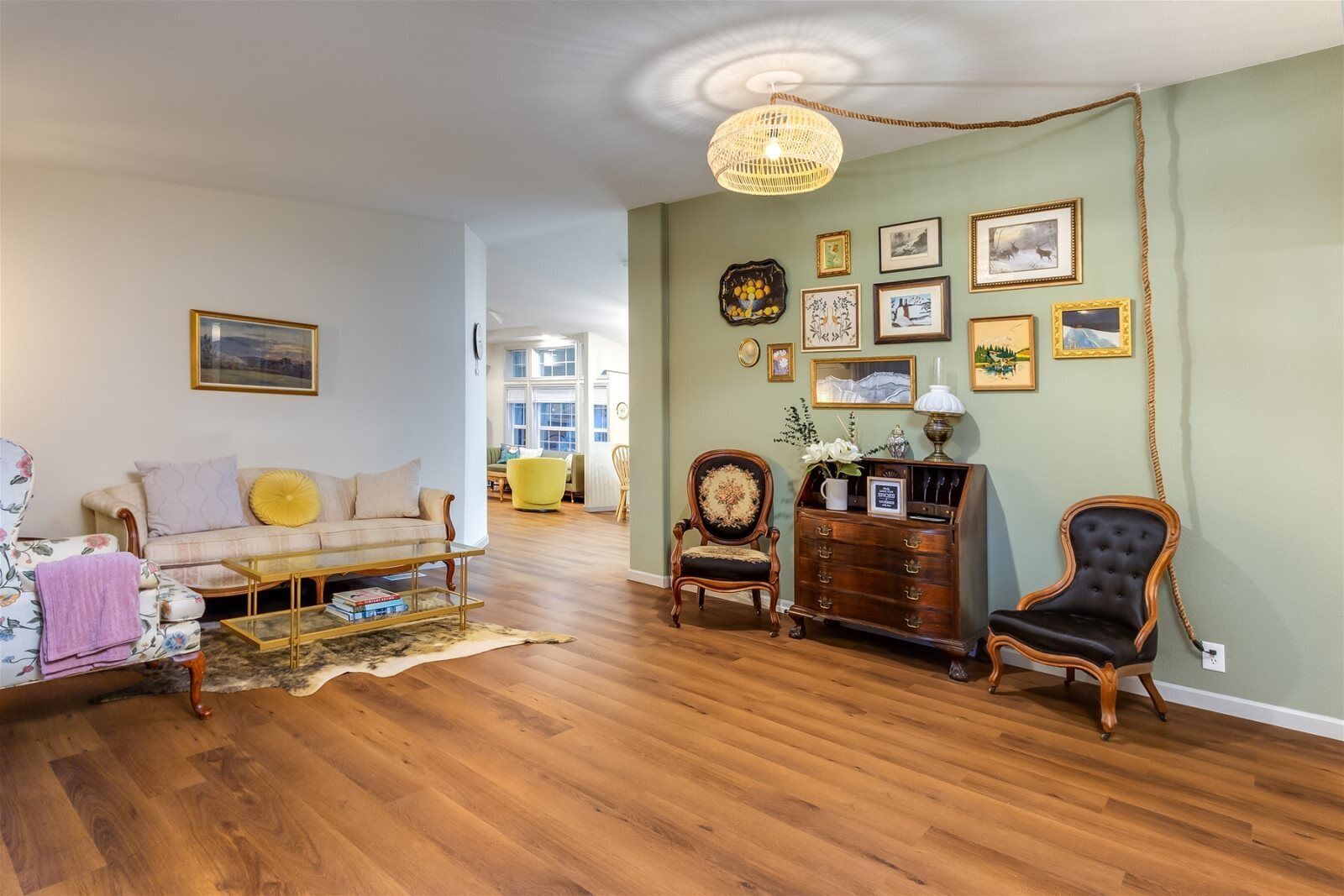 A spacious living room with hardwood flooring, a sofa, armchairs, a coffee table, and a wooden cabinet.