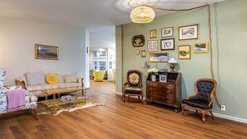 A spacious living room with hardwood flooring, a sofa, armchairs, a coffee table, and a wooden cabinet.