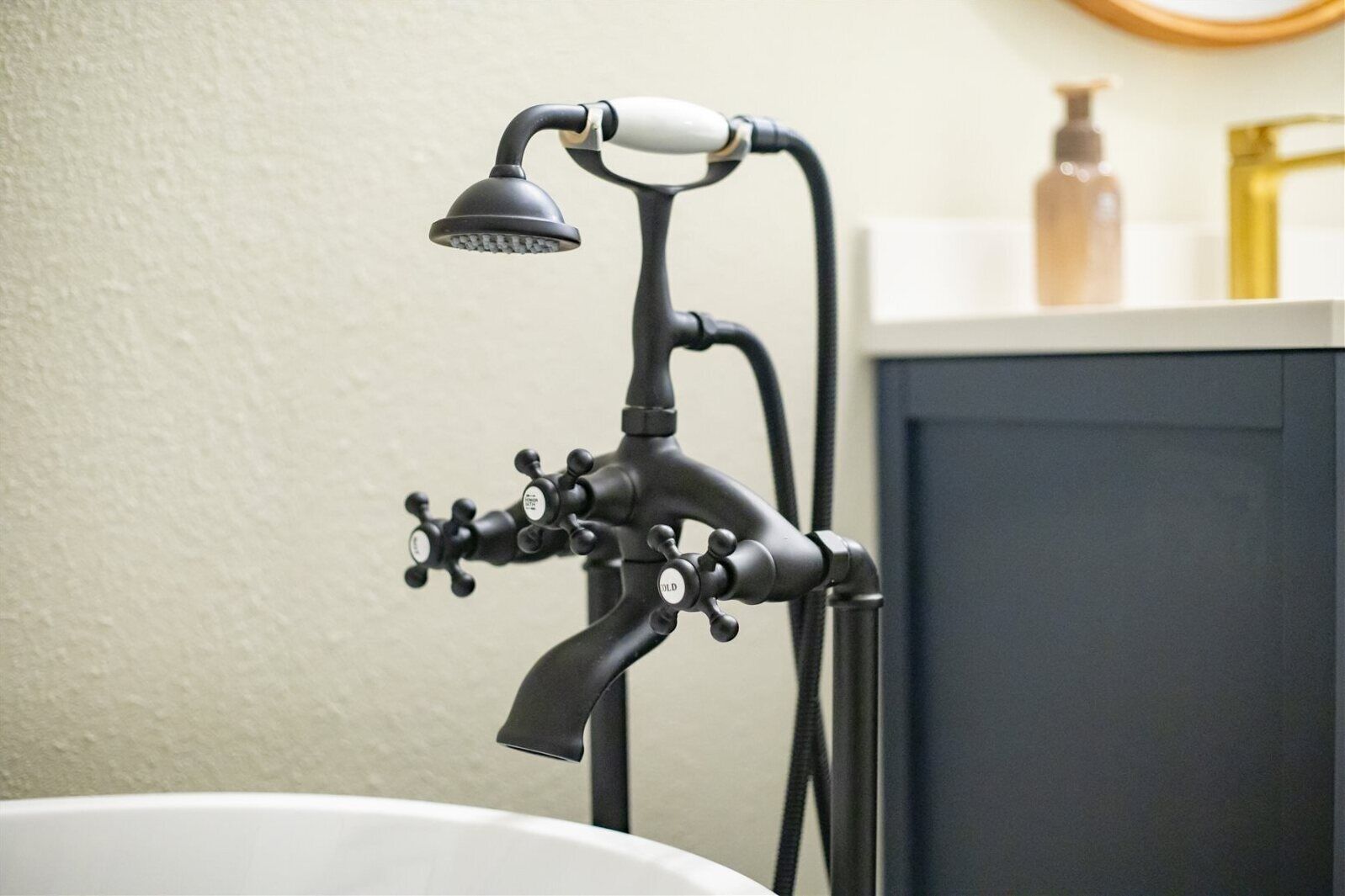 Un baño con un cabezal de ducha y grifo de estilo vintage en negro, una bañera blanca y un espejo con marco de madera sobre el lavabo.
