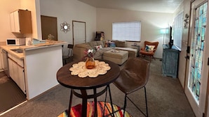 A compact living space with a kitchenette, a dining area with a table and chairs, a sofa, and a small armchair. - Clyde's Crib: Cozy Ms. Pac-Man (Boise)