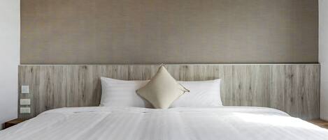 Una cama bien hecha con sábanas blancas y una manta color beige, cabecera de madera y dos lámparas fijadas a la pared.
