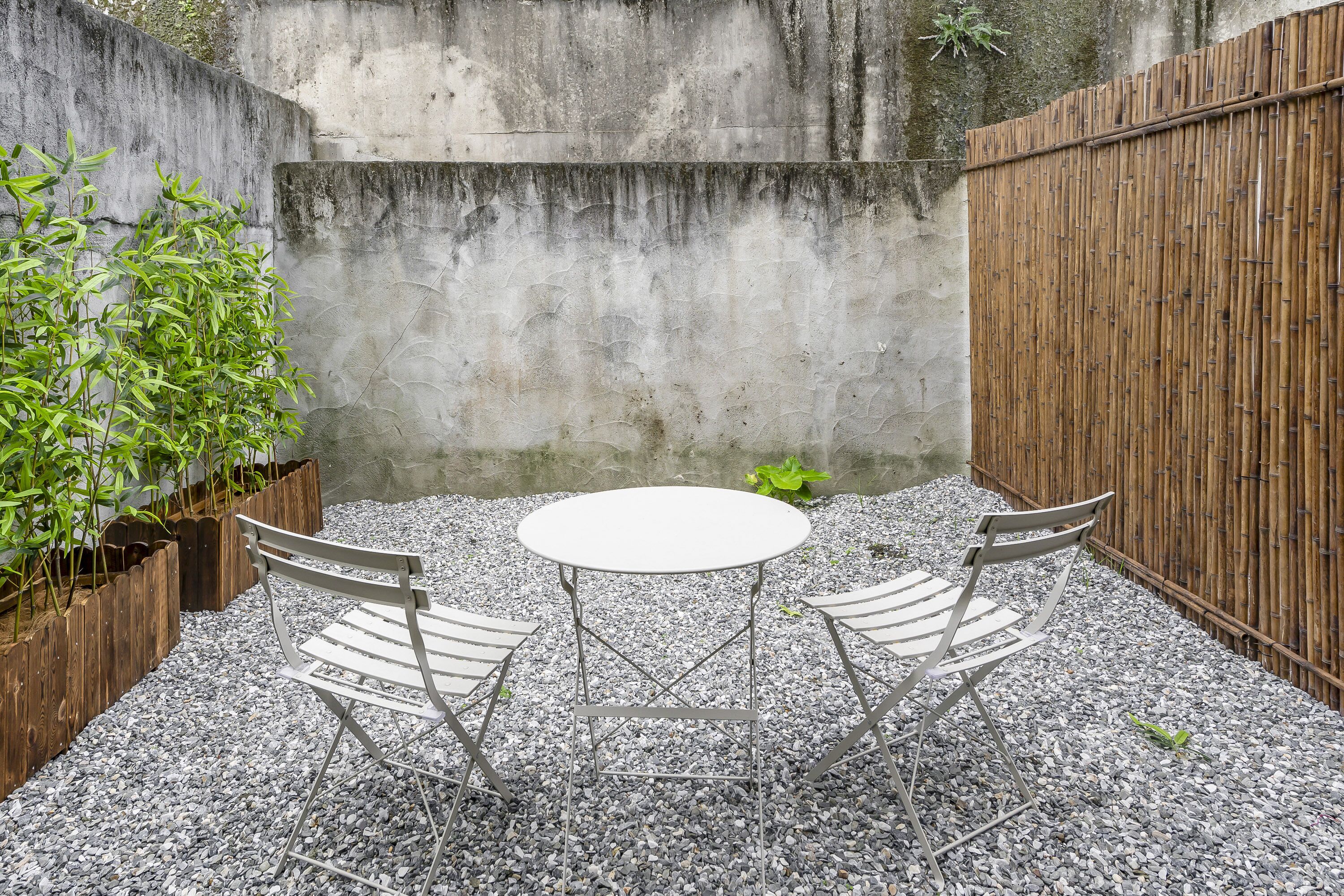 A patio with a round table and four chairs, surrounded by gravel and bamboo fencing.