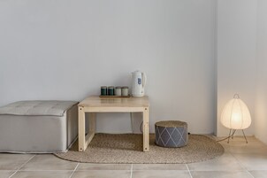Una habitación minimalista con una mesa de madera, un sofá gris, una alfombra pequeña, una lámpara y un hervidor.
