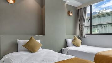 A hotel room with two beds, each with white bedding and a brown accent pillow. The room has a large window with a view of buildings and mountains.