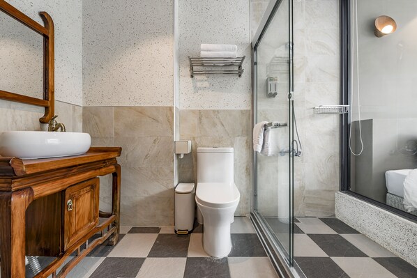 A bathroom with a wooden vanity, a toilet, a glass shower enclosure, and a tiled floor.