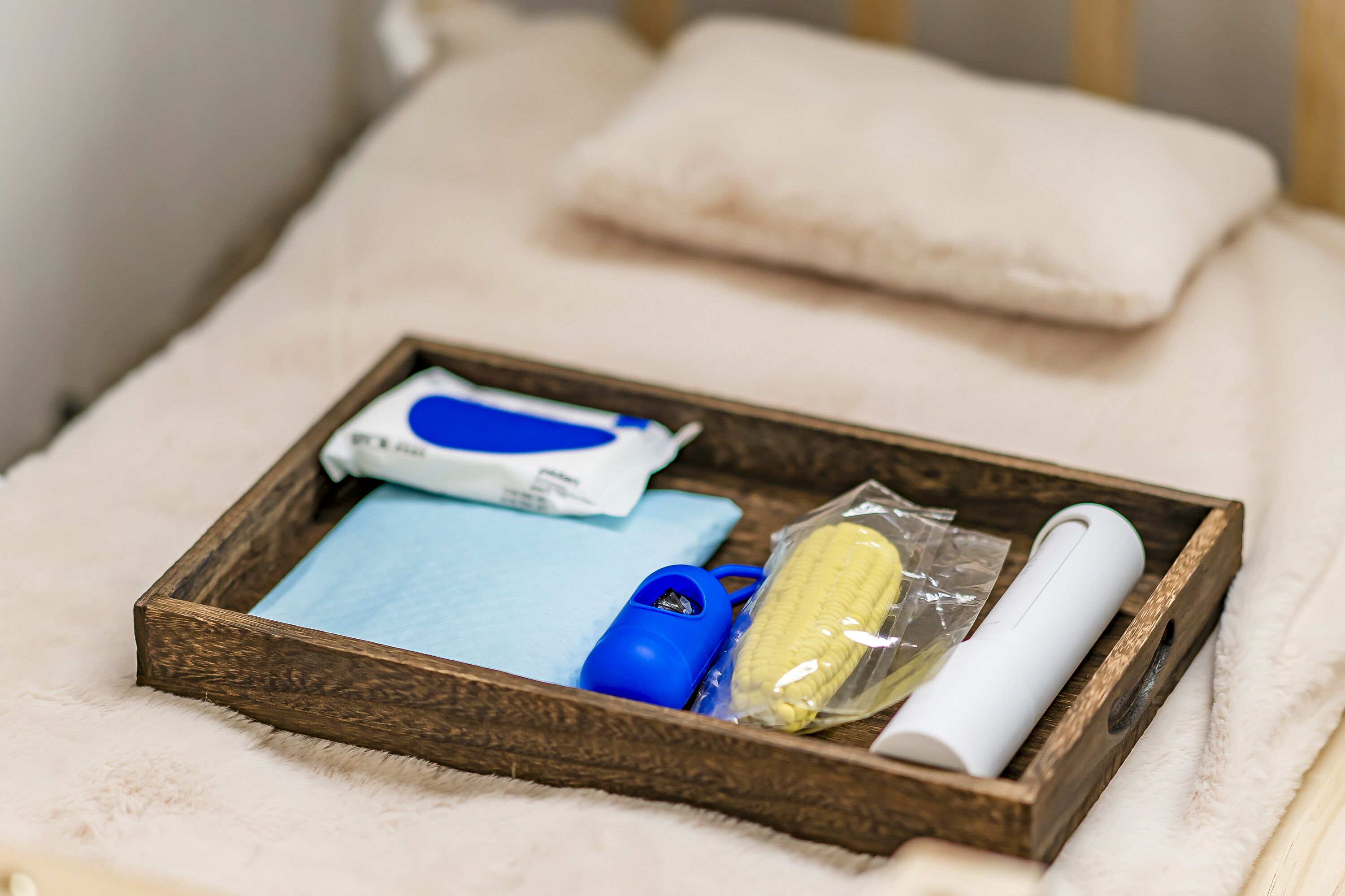 A wooden tray with a blue and white face mask, a blue hairdryer, a banana, and a white tube on a fluffy white surface.