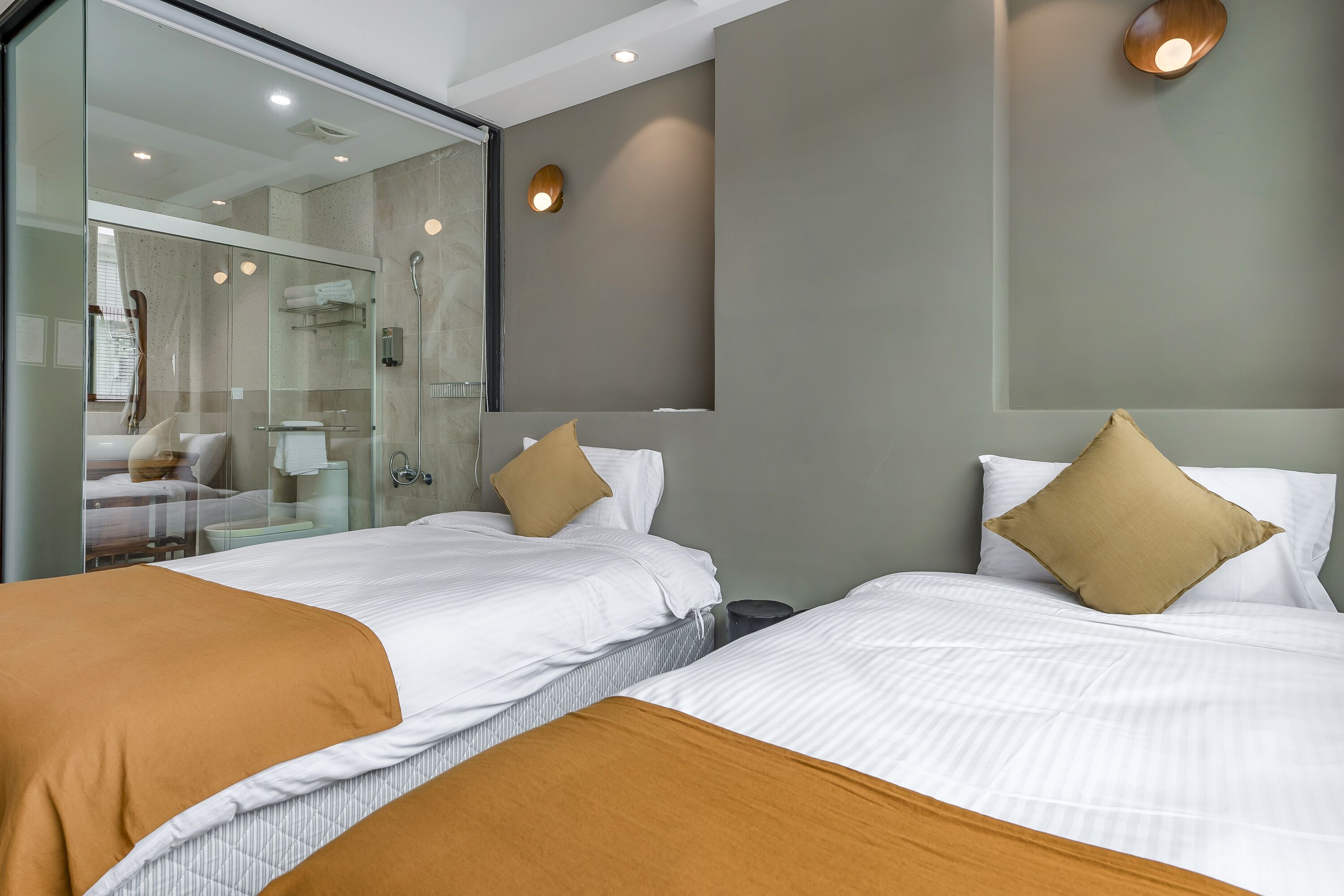 A hotel room with two beds, a glass shower enclosure, and a small sitting area with a table and chairs.