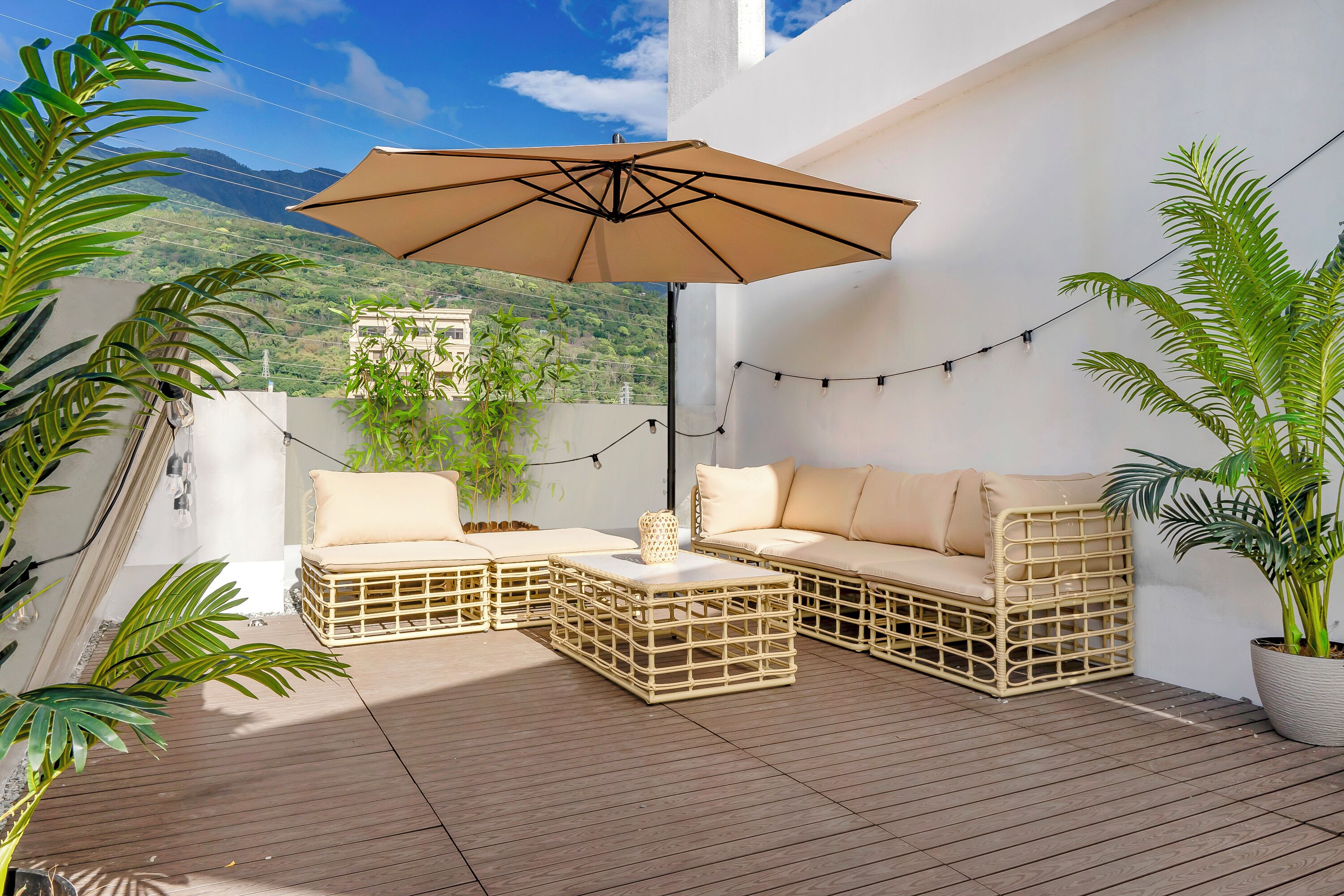 Un patio con muebles de mimbre, una sombrilla grande y luces de cadena.