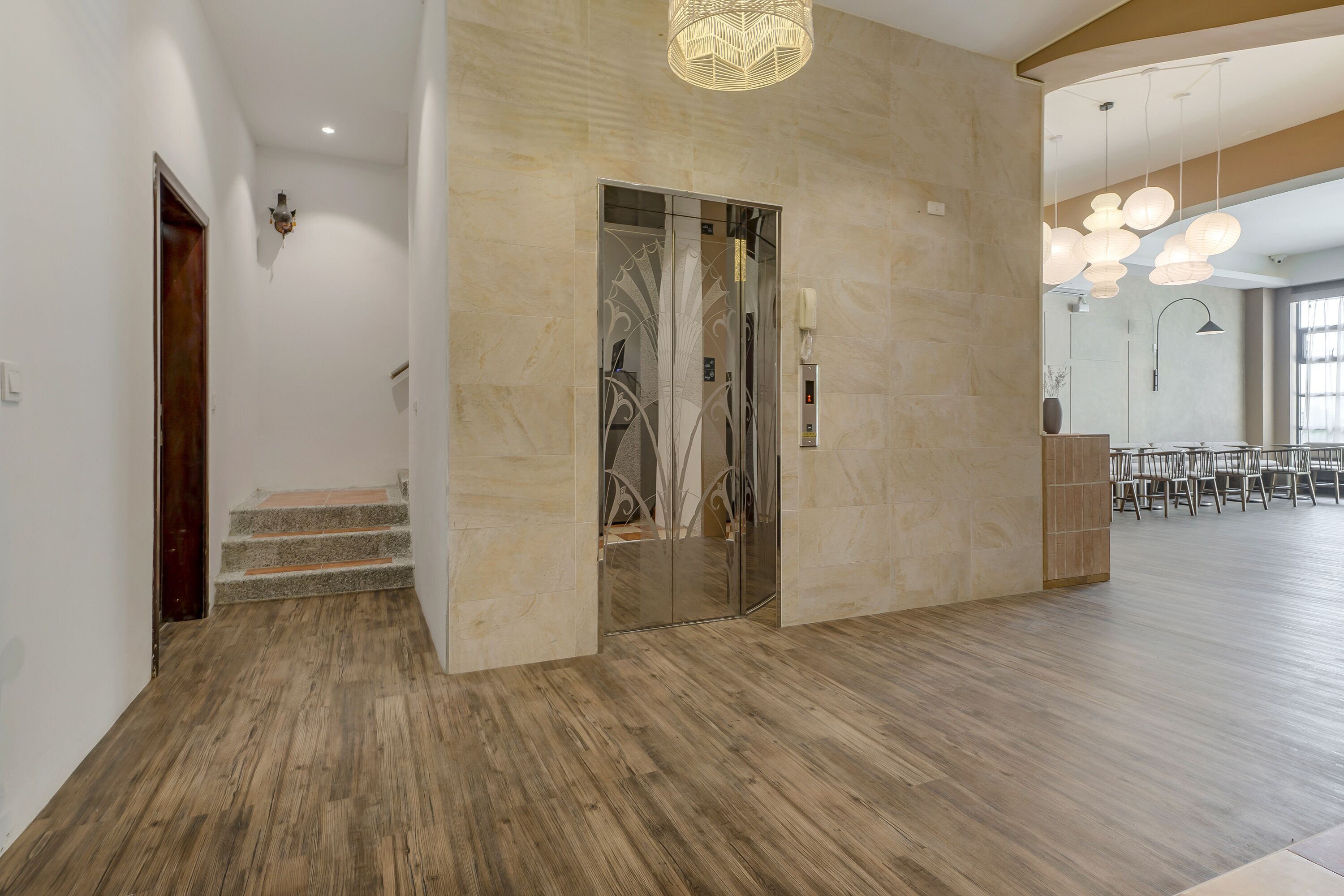A spacious lobby with a wooden floor, a glass elevator, and a seating area with chairs.