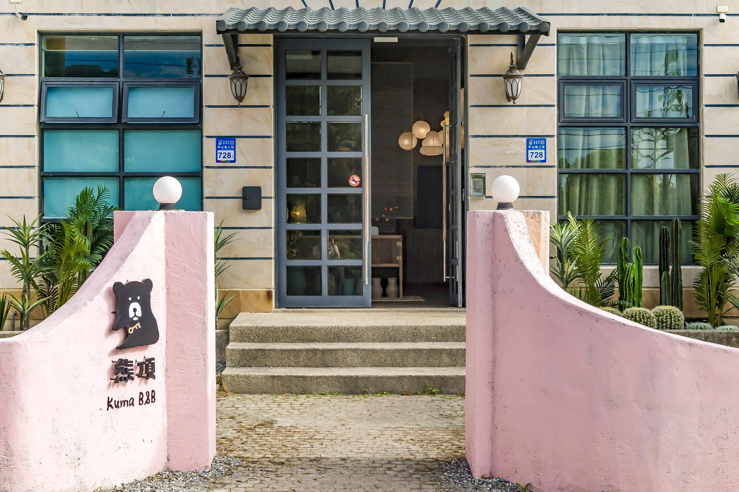 A building entrance with a glass door, a blue sign with the number 728, and a bear logo on a pink wall.