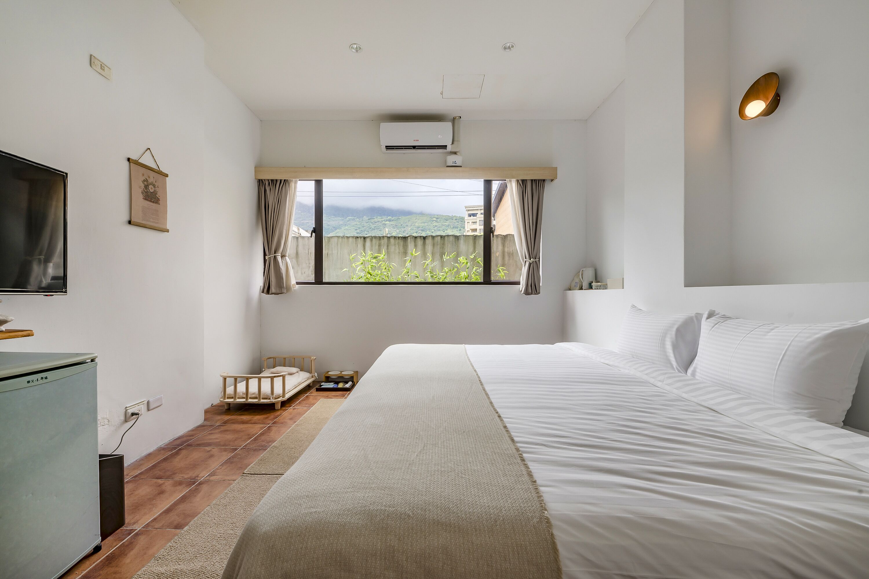 Quarto com cama grande, televisão, escrivaninha e janela com cortinas.