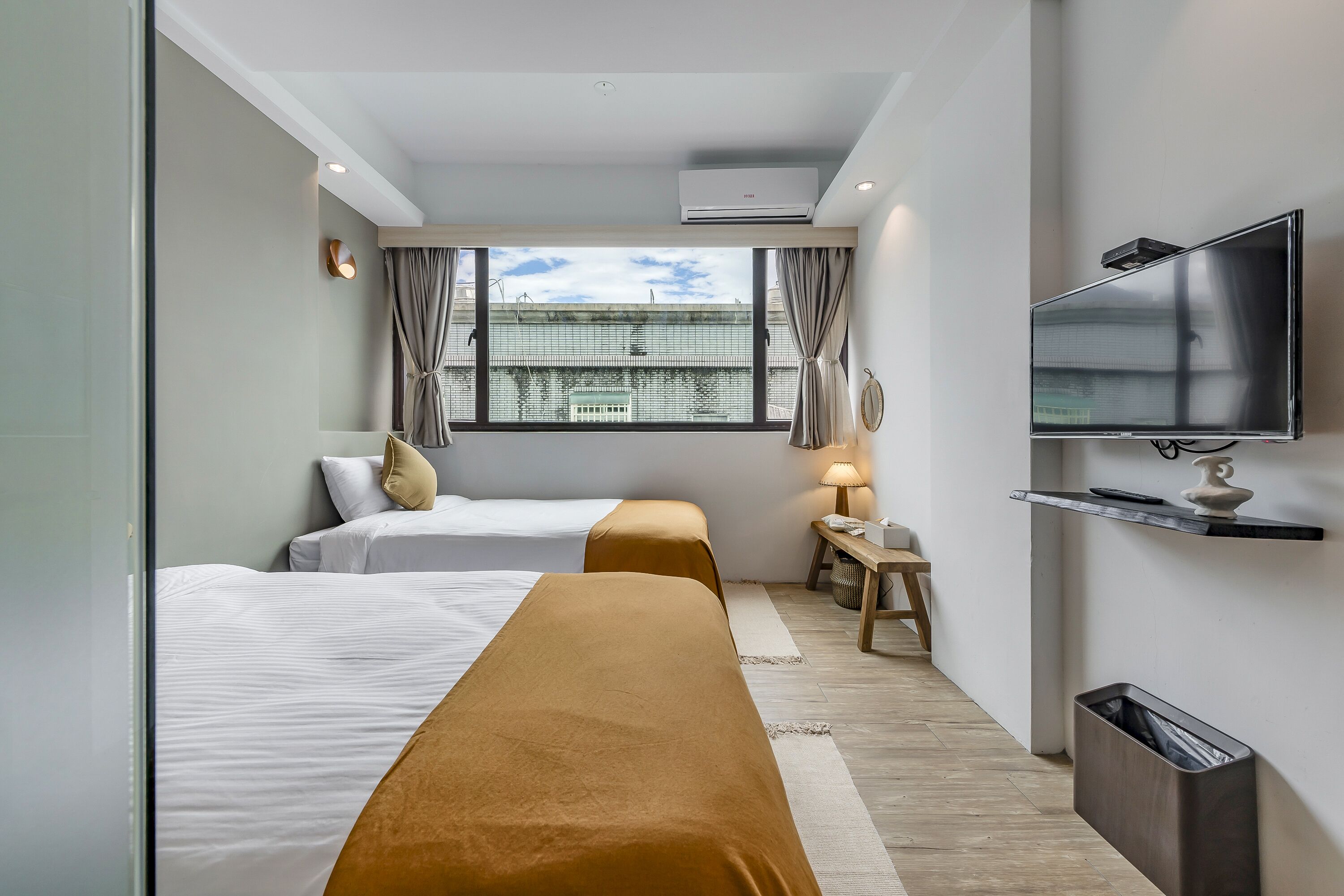 A hotel room with two beds, a TV, a desk with a lamp, and a window with curtains.