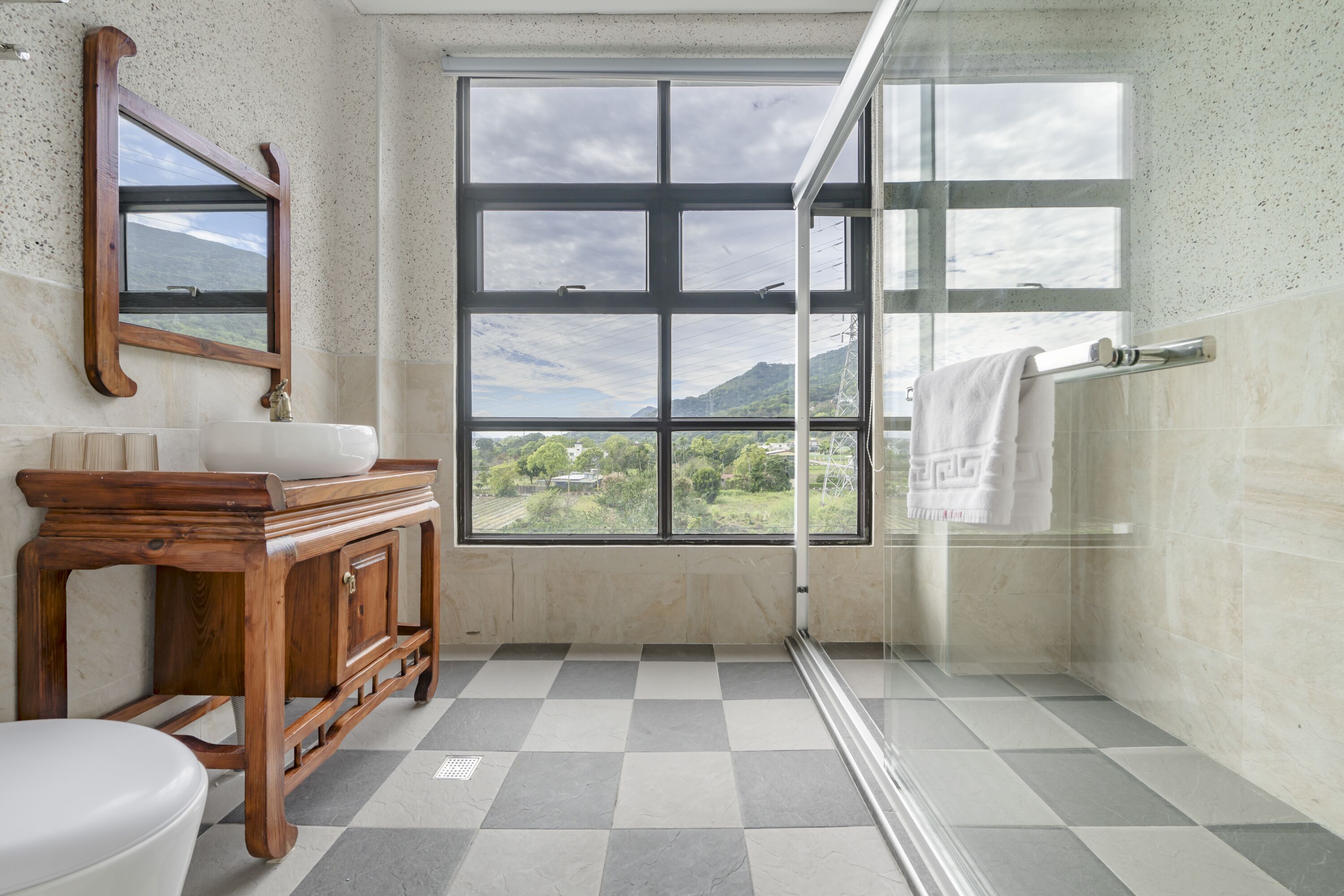 A bathroom with a large window, a wooden vanity, and a glass shower enclosure.