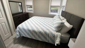 Quarto com cama, penteadeira e duas janelas.