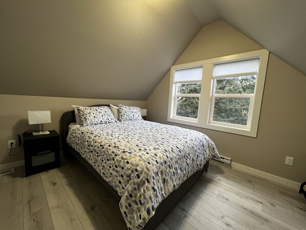 Un dormitorio con cama, mesita de noche, lámpara y ventana con persianas.