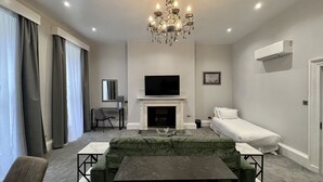 Een moderne woonkamer met een open haard, een flatscreen televisie, een groene bank en een kroonluchter.