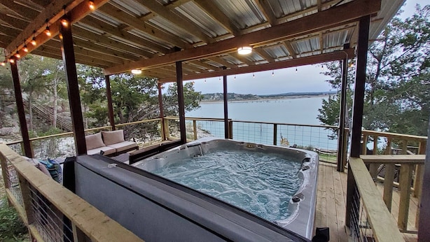 Een hottub met uitzicht op een meer, een houten terras en buitenzitplaatsen.